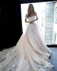 a woman in a wedding dress standing by a window with her hands on her hips