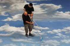 two men in black shirts are painting clouds with blue and white paint on the ground