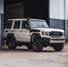 a white four door suv parked in front of a warehouse building with its doors open