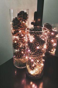 two glasses filled with pine cones sitting on top of a table next to each other