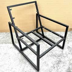 a black metal chair sitting on top of a white floor next to a tan wall