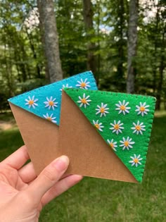 two pieces of paper with daisies on them are held up in front of some trees