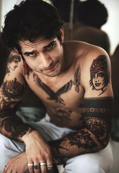 a shirtless man with tattoos on his arms and chest sitting in front of a mirror