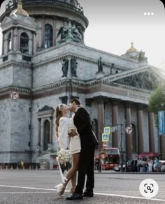 a newly married couple kissing in front of an old building on a city street,