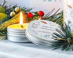 two candles sitting on top of a table next to tins filled with christmas decorations