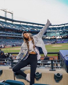 a woman sitting on top of a bench in front of a baseball field with her arms up