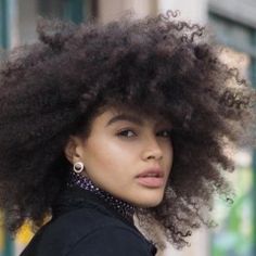 a close up of a person wearing a black jacket and an afro hairdo with large earrings