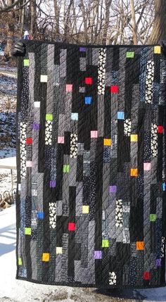 a black quilt hanging from the side of a tree in snow covered ground next to trees