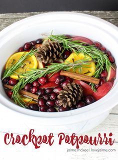 a white bowl filled with cranberries, oranges and pine cones on top of a wooden table