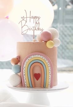 a birthday cake with a rainbow design on the top and balloons in the air behind it