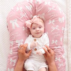 a woman holding a baby on top of a pink pillow with bows in it's hair