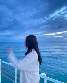 a woman standing on the side of a boat looking out over the ocean at dusk