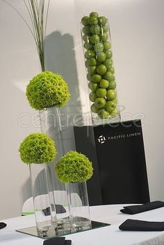 three vases filled with green flowers on top of a white table next to a black box