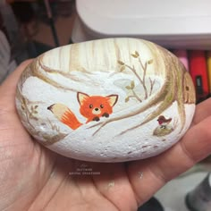 a hand holding a painted rock with a fox on it