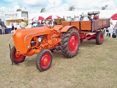 an orange tractor parked on top of a grass covered field next to people sitting in chairs