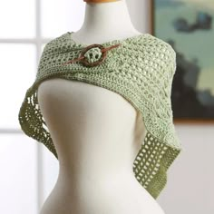 a white mannequin wearing a green crochet shawl