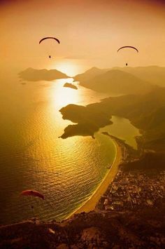 two parasailers are flying over the ocean at sunset