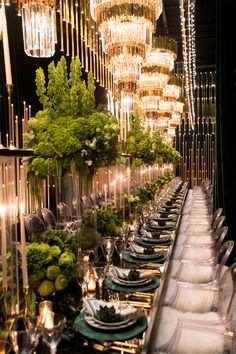 a long table is set with silverware and green place settings, surrounded by chandeliers