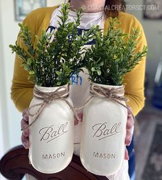 a woman holding two mason jars with plants in them