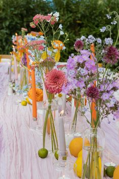 there are many vases with flowers and lemons on the long table cloth, along with candles