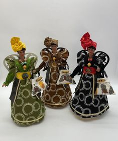 three figurines are standing next to each other on a white surface, one is wearing a green dress and the other has a red bow