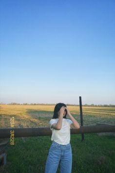 a woman standing in front of a fence with her hands to her face and looking through the binoculars