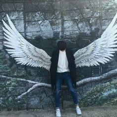 a man standing in front of a wall with wings painted on it