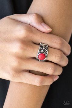 a woman's hand wearing a ring with a red stone in the middle and a black background