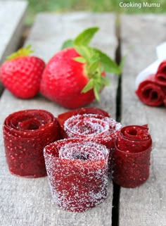 some strawberries are sitting on a wooden table next to rolled up red paper towels