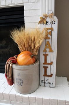 a white fireplace mantel with pumpkins and wheat stalks in a metal bucket next to a sign that reads hello fall