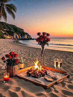 two glasses of wine are sitting on a tray with food and flowers in front of the ocean