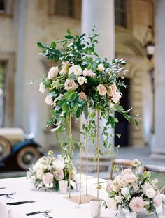 the table is set with white and pink flowers, greenery and gold candlesticks