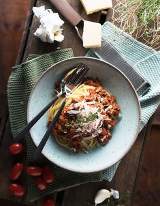 a plate of pasta with sauce, cheese and tomatoes on a table next to a knife and fork