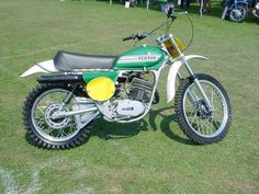 a green and white dirt bike parked on top of a grass covered field with people in the background