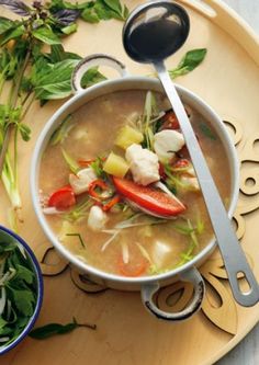 a bowl of soup on a plate with spoons and greens next to the bowl