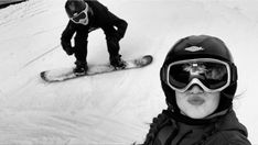 a man riding a snowboard down the side of a snow covered slope next to another person