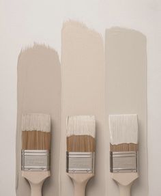 three paintbrushes are lined up against the wall with different shades of white on them