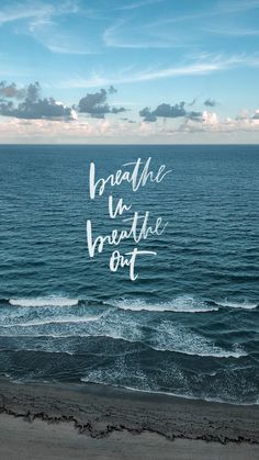 the words breathe and breathe out are written in white ink on an ocean beach with waves