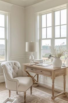 a white chair sitting next to a wooden desk in front of two large windows on top of a hard wood floor