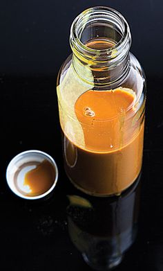 a glass jar filled with orange liquid next to a small white cup on a black surface