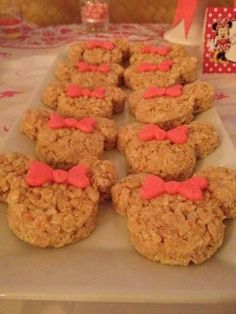 some cookies with pink bows are on a white platter at a minnie mouse party