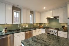 a kitchen with white cabinets and green marble counter tops, stainless steel appliances and dishwasher