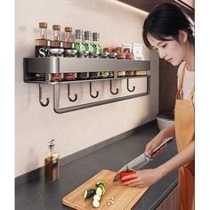 a woman cutting up vegetables on top of a wooden cutting board in front of a wall mounted spice rack