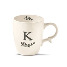 a white coffee cup with the letter k on it's side and leaves in the middle