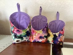 three purple and white flowered purses sitting on top of a wooden table