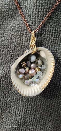 a shell with various beads in it sitting on a gray cloth covered surface, next to a gold filled chain