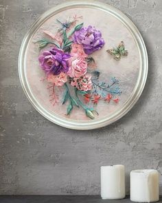 two candles are sitting on a table next to a wall with flowers and butterflies painted on it