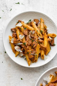 two bowls filled with pasta and meat on top of a white countertop next to another bowl full of food