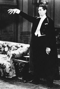 a black and white photo of a man in a suit pointing at something on the floor