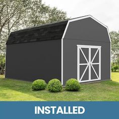 a large gray barn with the words insulated on it and three bushes in front